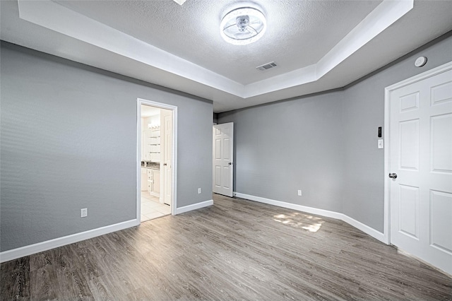 3019 Lela St, Irving, TX 75061 - unfurnished bedroom with a textured ceiling, wood finished floors, a raised ceiling, and connected bathroom
