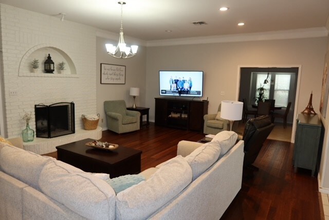 3035 Briarwood Dr, Paris, TX 75460 - living area with wood finished floors, a brick fireplace, a chandelier, ornamental molding, and recessed lighting