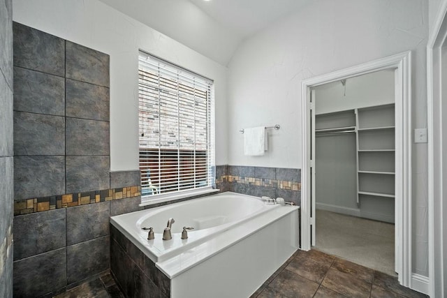 2425 Sir Lovel Ln, Lewisville, TX 75056 - full bathroom featuring a bath, a walk in closet, lofted ceiling, tile walls, and stone finish floors