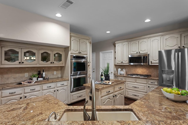 1817 Foxborough Trl, Flower Mound, TX 75028 - kitchen featuring appliances with stainless steel finishes, a sink, decorative backsplash, glass insert cabinets, and light stone counters