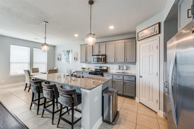 1317 Roadrunner Dr, Little Elm, TX 75068 - kitchen with stainless steel appliances, gray cabinets, a sink, light stone countertops, and a breakfast bar area