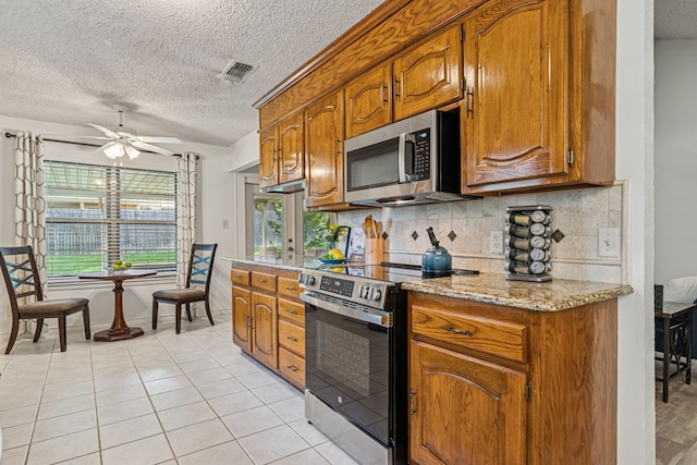 140 Amory Dr, Benbrook, TX 76126 - kitchen with stainless steel appliances, a textured ceiling, tasteful backsplash, brown cabinetry, and a ceiling fan