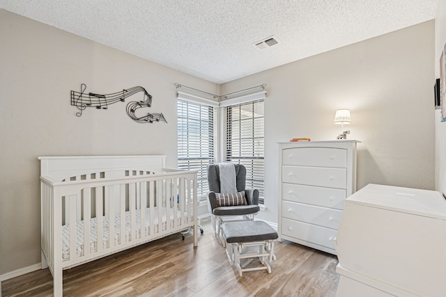 140 Amory Dr, Benbrook, TX 76126 - bedroom with wood finished floors, a textured ceiling, baseboards, and a nursery area