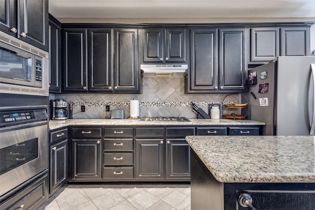 8405 White Stallion Trl, Mckinney, TX 75070 - kitchen featuring appliances with stainless steel finishes, under cabinet range hood, decorative backsplash, dark cabinets, and light tile patterned floors