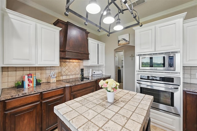 1225 County Road 1021, Burleson, TX 76028 - kitchen with stainless steel appliances, custom exhaust hood, decorative backsplash, arched walkways, and white cabinets