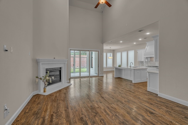 7819 Uxbridge Dr, Irving, TX 75063 - unfurnished living room with a ceiling fan, baseboards, dark wood-style flooring, a glass covered fireplace, and a towering ceiling
