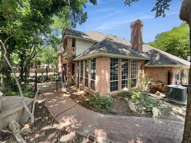 6029 Bellaire Dr, Benbrook, TX 76132 - view of side of property featuring central AC unit, brick siding, roof with shingles, and a chimney