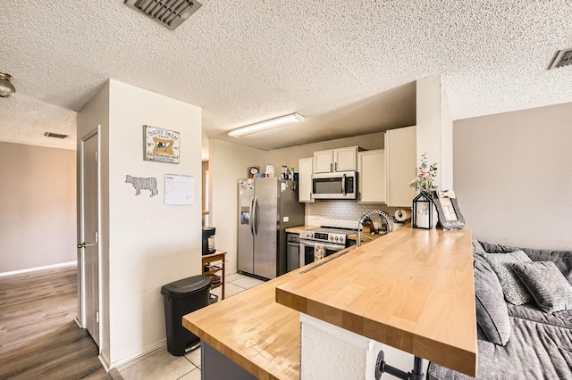 1806 Willowbrook Dr, Terrell, TX 75160 - kitchen with stainless steel appliances, butcher block counters, decorative backsplash, a textured ceiling, and a peninsula
