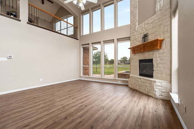 10205 Fairway Vista Dr, Rowlett, TX 75089 - unfurnished living room featuring a ceiling fan, baseboards, wood finished floors, a stone fireplace, and a towering ceiling
