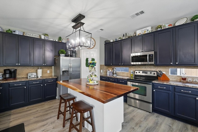 2304 Ranch House Dr, Denton, TX 76210 - kitchen featuring appliances with stainless steel finishes, butcher block countertops, light wood finished floors, tasteful backsplash, and a breakfast bar area