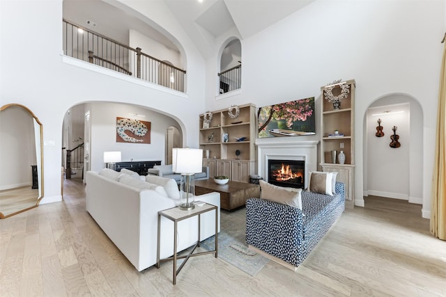 2880 Meadow Dell Dr, Prosper, TX 75078 - living room with light wood-type flooring, a glass covered fireplace, a towering ceiling, baseboards, and arched walkways