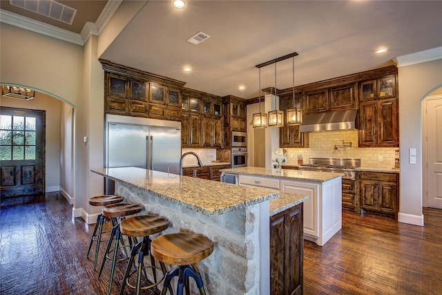 552 Horseshoe Bnd, Royse City, TX 75189 - kitchen featuring under cabinet range hood, an island with sink, built in appliances, dark wood finished floors, and crown molding