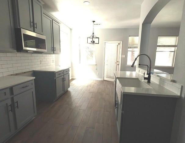 1207 Goldeneye, Aubrey, TX 76227 - kitchen with stainless steel microwave, a sink, dark wood finished floors, decorative backsplash, and gray cabinets