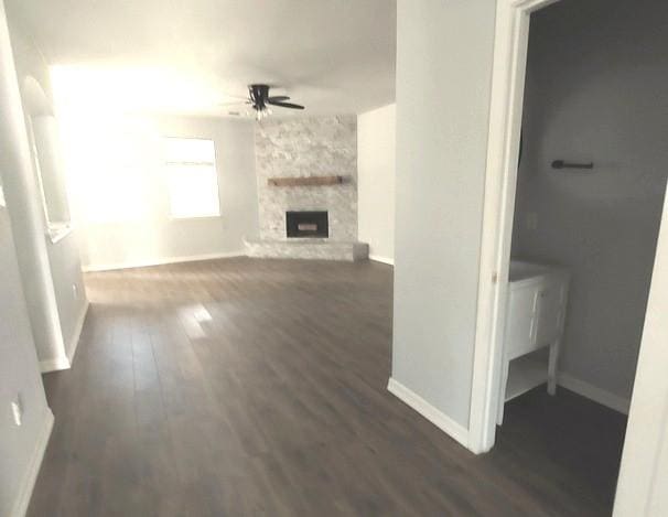 1207 Goldeneye, Aubrey, TX 76227 - unfurnished living room with ceiling fan, dark wood-style floors, baseboards, and a stone fireplace