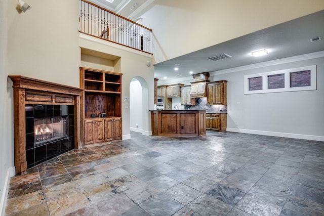 3317 S Riley Ct, Hurst, TX 76054 - unfurnished living room with stone tile floors, crown molding, a glass covered fireplace, arched walkways, and baseboards