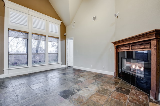 3317 S Riley Ct, Hurst, TX 76054 - unfurnished living room featuring a glass covered fireplace, baseboards, stone tile floors, and high vaulted ceiling