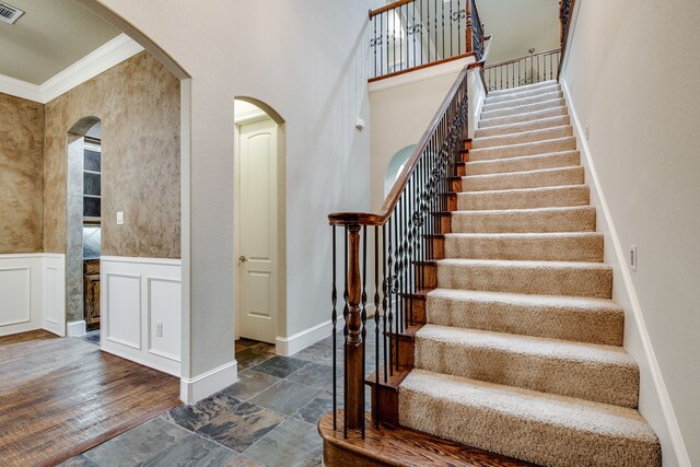 3317 S Riley Ct, Hurst, TX 76054 - stairway featuring stone finish floors, crown molding, arched walkways, and wainscoting
