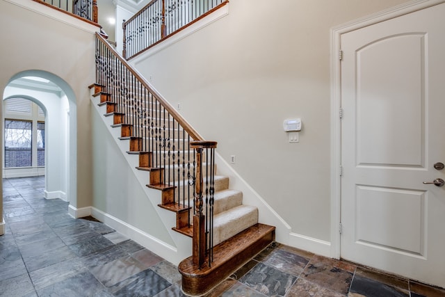 3317 S Riley Ct, Hurst, TX 76054 - staircase featuring stone tile flooring, arched walkways, baseboards, and a towering ceiling
