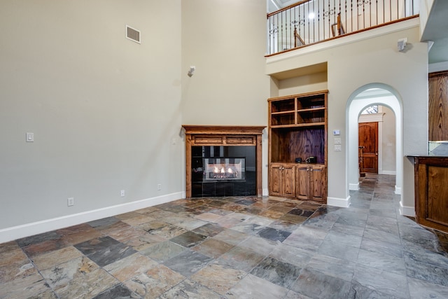 3317 S Riley Ct, Hurst, TX 76054 - unfurnished living room featuring stone tile flooring, a towering ceiling, arched walkways, baseboards, and a tile fireplace