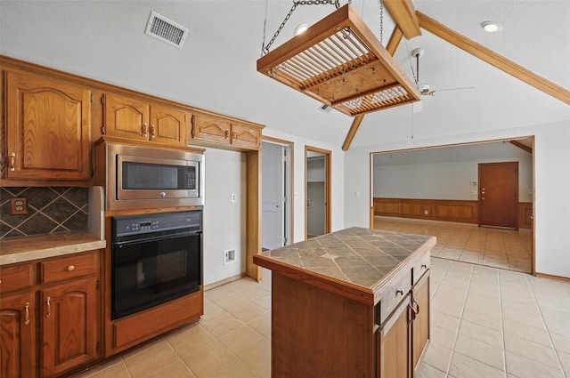 1521 Treeline Dr, Desoto, TX 75115 - kitchen featuring oven, stainless steel microwave, tile countertops, wainscoting, and backsplash