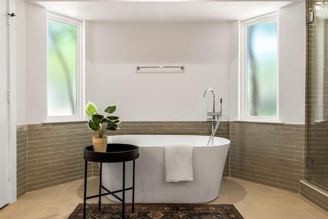 2626 Club Meadow Dr, Garland, TX 75043 - bathroom featuring tile walls, a freestanding bath, a wainscoted wall, tile patterned flooring, and healthy amount of natural light