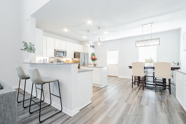 2049 Hartley Dr, Forney, TX 75126 - kitchen with appliances with stainless steel finishes, a peninsula, light wood-type flooring, a kitchen breakfast bar, and white cabinetry
