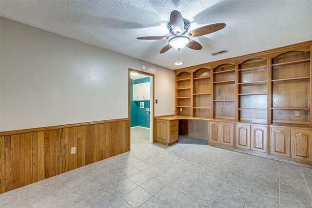 6400 Kingswood Dr, Fort Worth, TX 76133 - empty room featuring a textured ceiling, a ceiling fan, a wainscoted wall, wood walls, and light tile patterned floors
