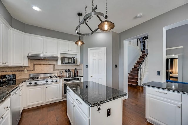1529 Arrowhead Ln, Carrollton, TX 75007 - kitchen with stainless steel appliances, under cabinet range hood, dark wood-style flooring, white cabinetry, and decorative backsplash
