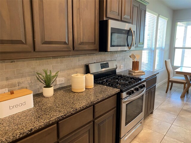 1037 Madelia Ave, Fort Worth, TX 76177 - kitchen featuring stainless steel appliances, decorative backsplash, light tile patterned floors, dark stone countertops, and baseboards