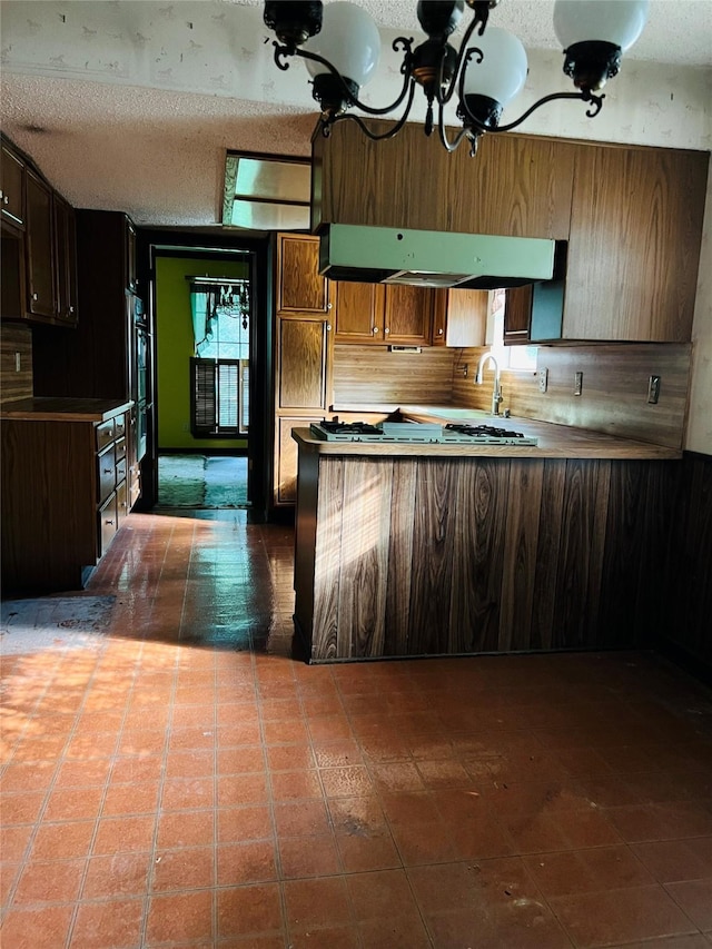 425 Ten Mile Dr, Desoto, TX 75115 - kitchen with a peninsula, a sink, a chandelier, a textured ceiling, and under cabinet range hood