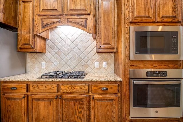 2636 Deer Hollow Dr, Little Elm, TX 75068 - kitchen featuring appliances with stainless steel finishes, backsplash, brown cabinets, and light stone countertops