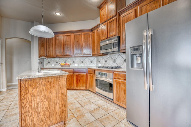 6939 Truth Dr, Dallas, TX 75236 - kitchen featuring appliances with stainless steel finishes, a sink, backsplash, a kitchen island with sink, and brown cabinets