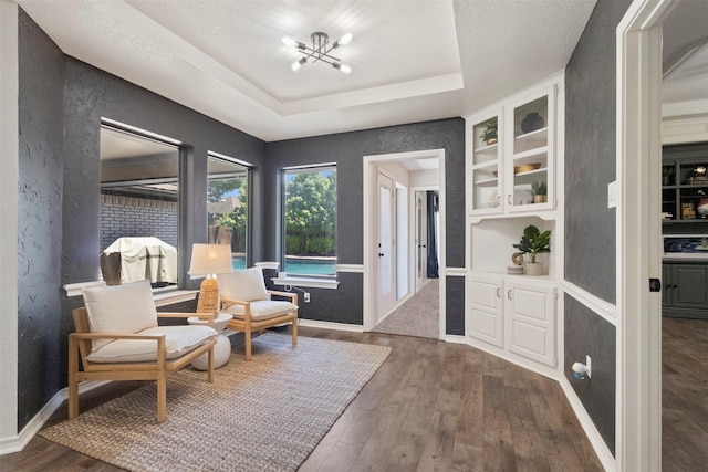 517 Sunset Dr, Hurst, TX 76054 - living area featuring wood finished floors, a chandelier, a tray ceiling, baseboards, and built in shelves