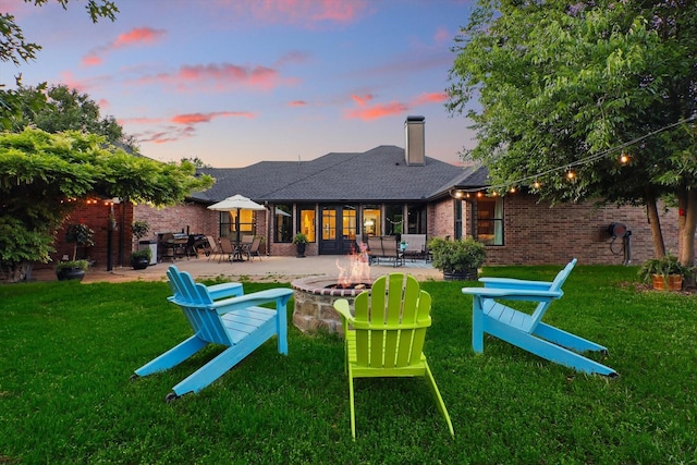 1208 Chandler Cir, Prosper, TX 75078 - back of house at dusk featuring an outdoor fire pit, a patio, a chimney, brick siding, and a yard