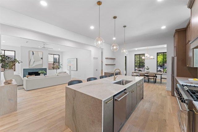 4516 Shenandoah Ave, University Park, TX 75205 - kitchen featuring stainless steel appliances, a sink, a center island with sink, light wood-style floors, and hanging light fixtures