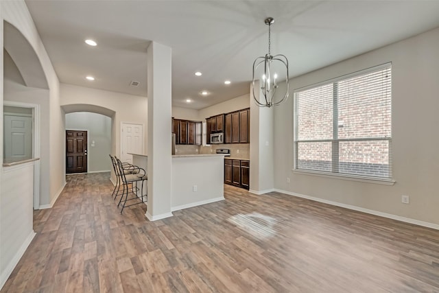 1804 Shoebill Dr, Little Elm, TX 75068 - kitchen with stainless steel microwave, dark brown cabinets, arched walkways, light wood-style flooring, and light countertops