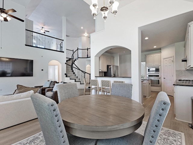 2231 Cold Water Dr, Prosper, TX 75078 - dining room featuring arched walkways, a ceiling fan, light wood-style floors, stairway, and a towering ceiling