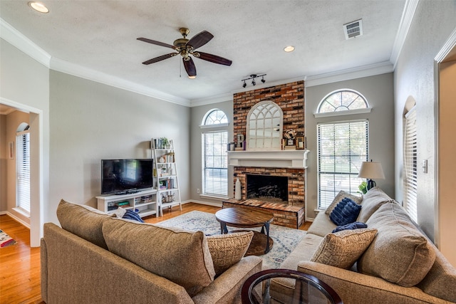 2332 Heatherwoods Way, Carrollton, TX 75007 - living room featuring a ceiling fan, light wood-style floors, crown molding, a fireplace, and a textured ceiling