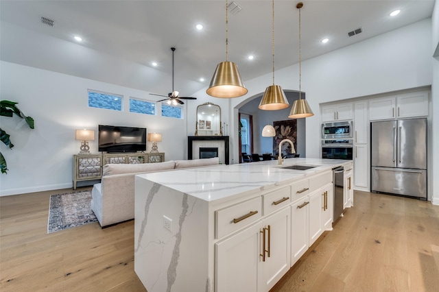 3201 Sunday Silence Ln, Celina, TX 75009 - kitchen featuring appliances with stainless steel finishes, a sink, light wood-style flooring, ceiling fan, and a tiled fireplace