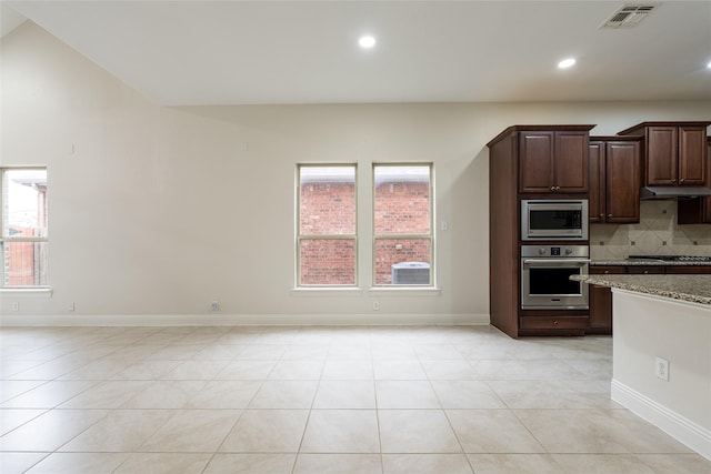 10909 Blake Gdns, Mckinney, TX 75072 - kitchen with stainless steel appliances, light stone counters, backsplash, light tile patterned flooring, and baseboards