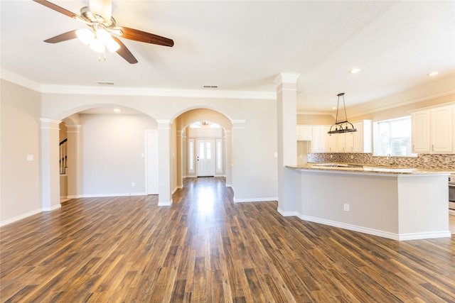 3015 Oak Dr, Rockwall, TX 75032 - unfurnished living room featuring arched walkways, ornate columns, ceiling fan, dark wood finished floors, and crown molding