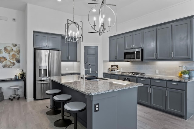 1805 13th St, Argyle, TX 76226 - kitchen featuring appliances with stainless steel finishes, a sink, light stone counters, a chandelier, and light wood-type flooring