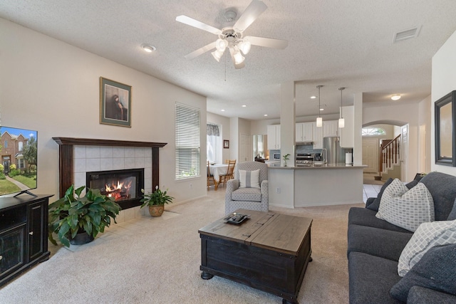 3942 Luke Ln, Carrollton, TX 75007 - living area featuring light carpet, a tiled fireplace, ceiling fan, arched walkways, and a textured ceiling