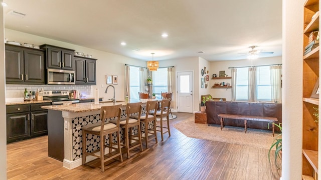 1715 Swale Ln, Granbury, TX 76049 - kitchen with appliances with stainless steel finishes, light wood-style floors, a sink, a breakfast bar area, and recessed lighting
