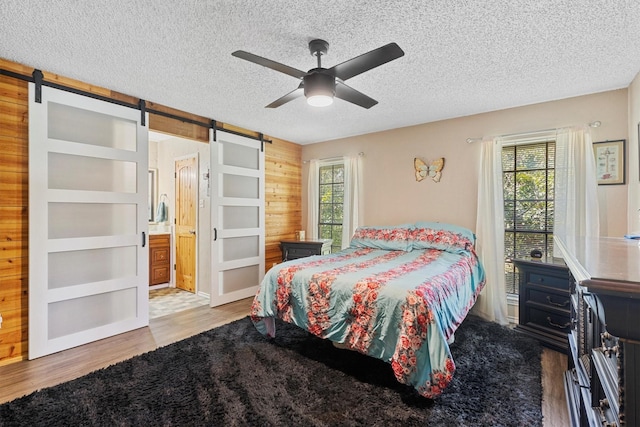 5240 Hill Ridge Dr, Fort Worth, TX 76135 - bedroom with a barn door, wooden walls, a textured ceiling, wood finished floors, and ceiling fan