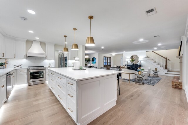6702 Rolling Vista Dr, Dallas, TX 75248 - kitchen featuring appliances with stainless steel finishes, custom exhaust hood, a kitchen island, light wood-type flooring, and white cabinets