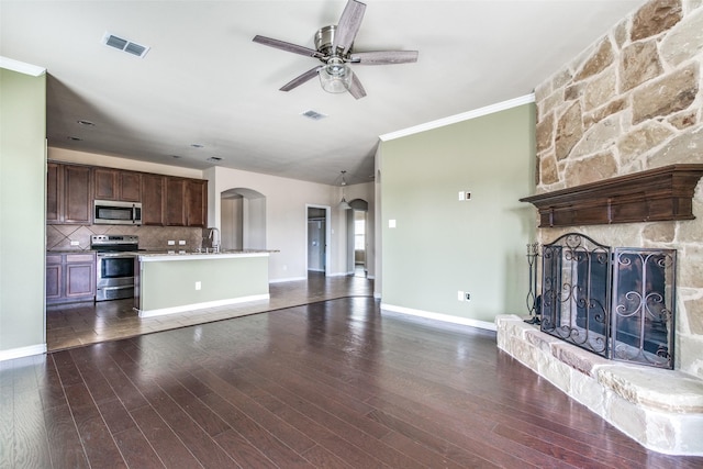 2520 Sabine Cir, Royse City, TX 75189 - unfurnished living room with arched walkways, a ceiling fan, ornamental molding, a stone fireplace, and dark wood-type flooring