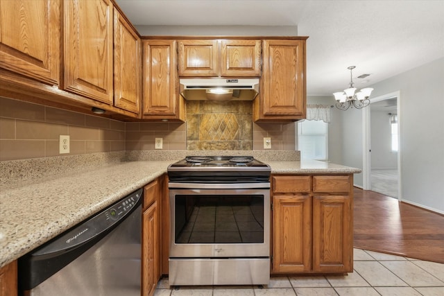 2311 Markland St, Irving, TX 75060 - kitchen featuring appliances with stainless steel finishes, under cabinet range hood, brown cabinetry, a chandelier, and decorative backsplash