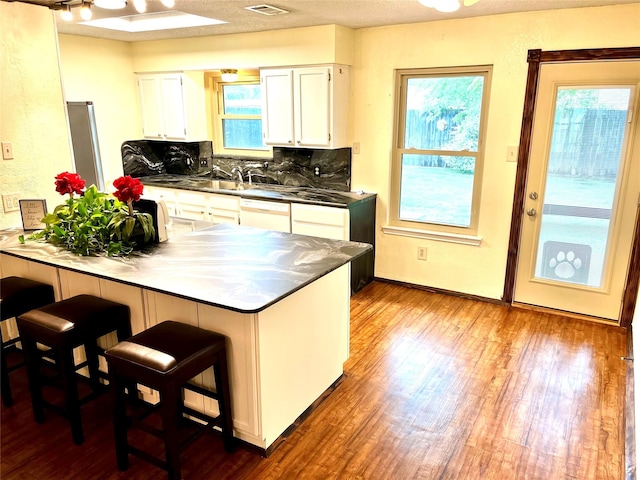 617 Reed St, Roanoke, TX 76262 - kitchen with dark countertops, dark wood-style flooring, a peninsula, white cabinetry, and a breakfast bar