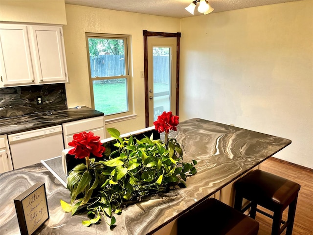 617 Reed St, Roanoke, TX 76262 - kitchen with white dishwasher, white cabinets, wood finished floors, dark countertops, and a breakfast bar area